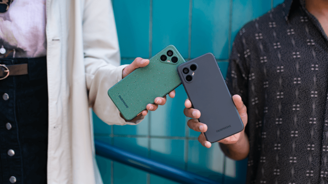 Two individuals holding Fairphone devices, one green and one black, showcasing the phone's design and color options